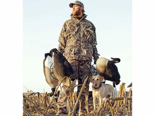 hunter  and a dog in a field wearing camo outfit and hat holding three decoys 