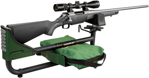 Black rifle with scope displayed  on green and black adjustable shooting rest with green bag