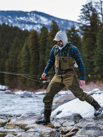 fisherman with pole in bib waders in stream 